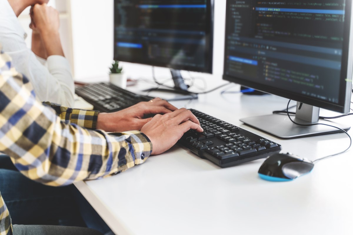 برنامه‌نویس در حال نوشتن کد روی دو مانیتور؛ نمونه‌کار عملی برای اپلای ارشد کامپیوتر